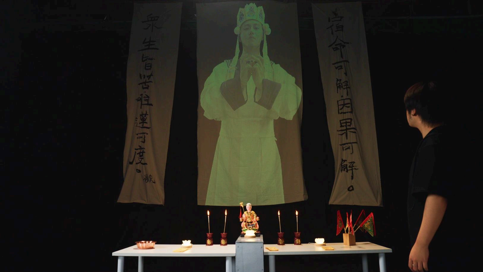 The 䝞 installation with a projected ritual figure, altar, candles and a viewer