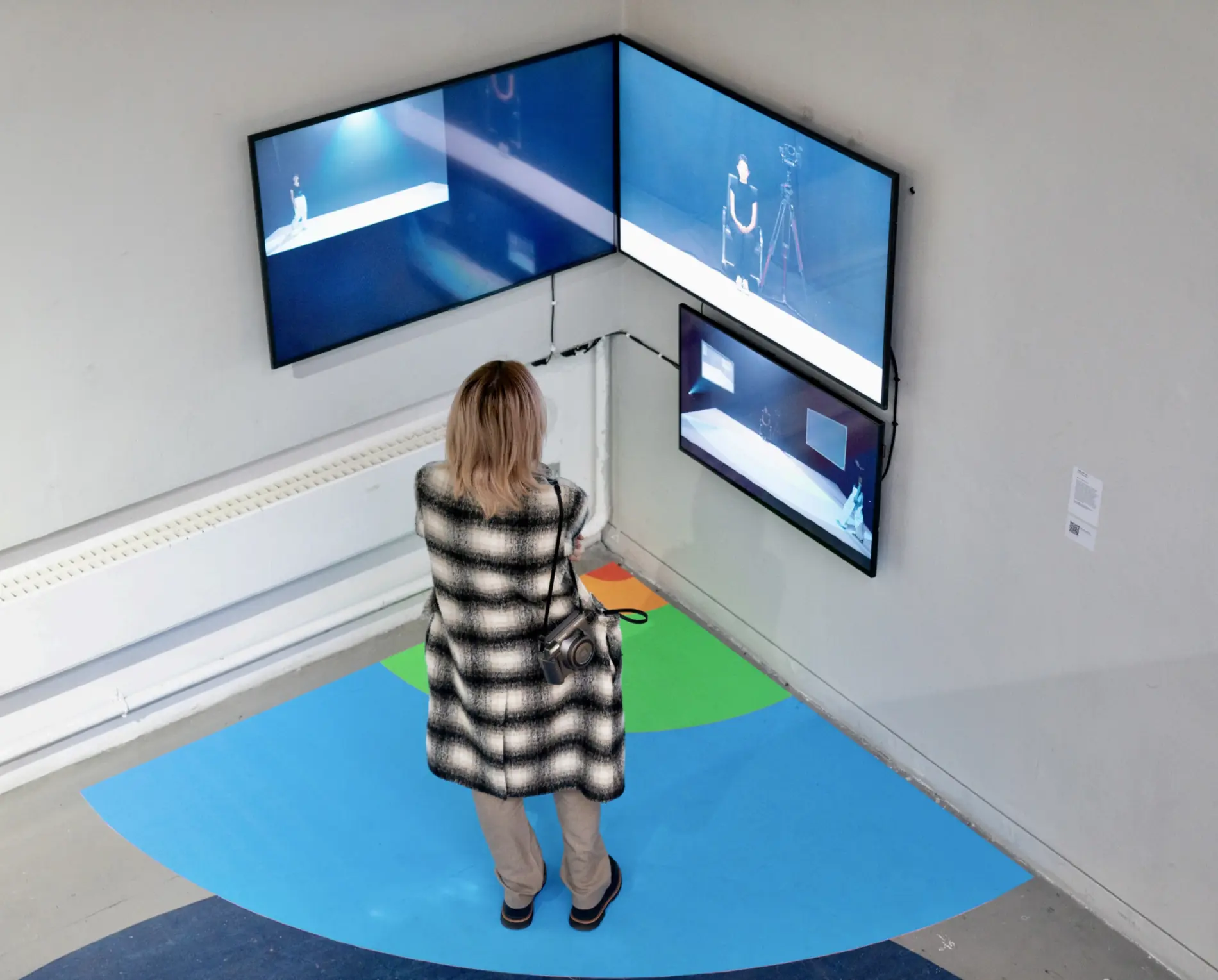 A visitor standing within the coloured floor field and watching the three screens