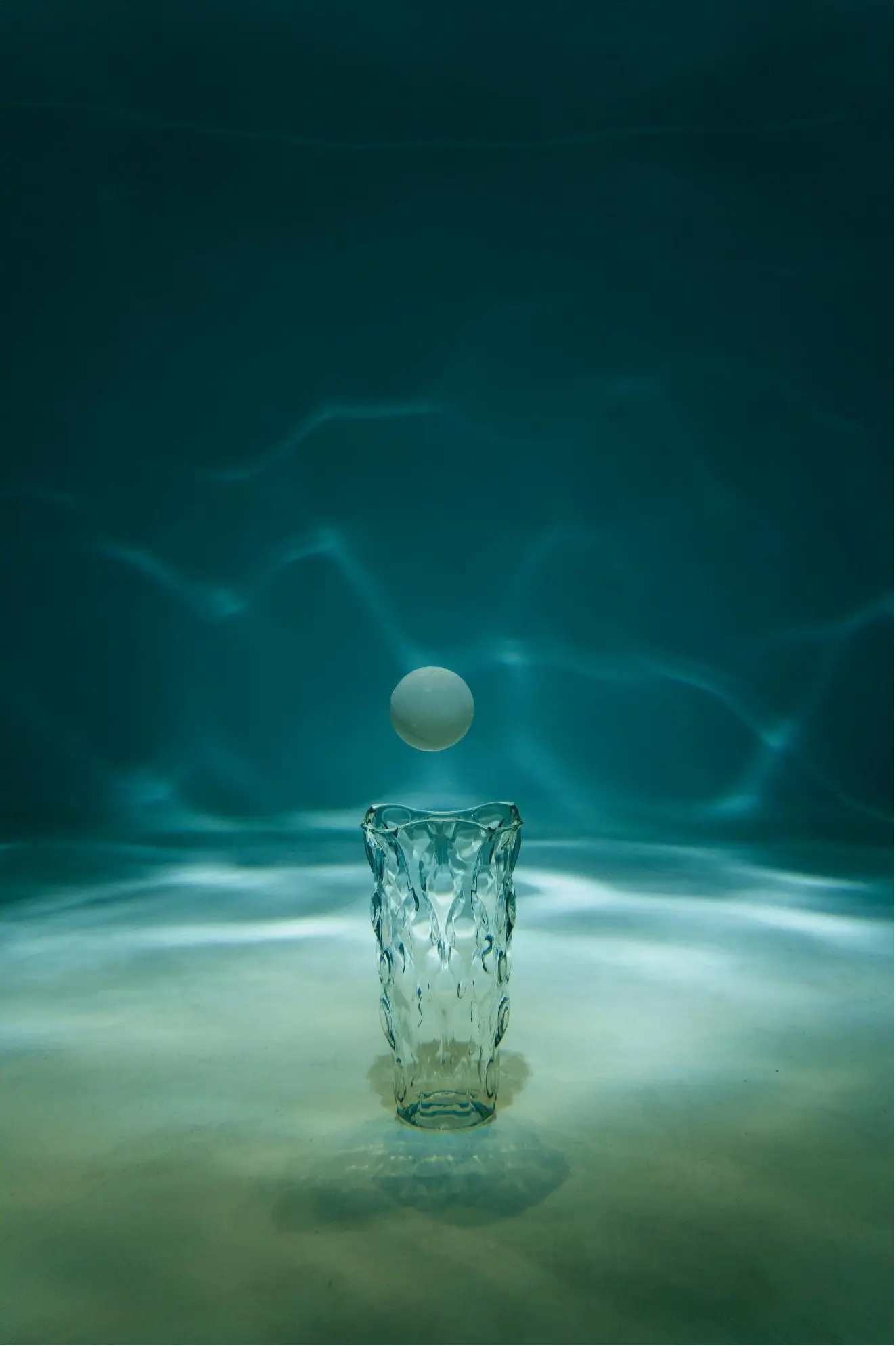 A pale sphere suspended directly above a glass vessel